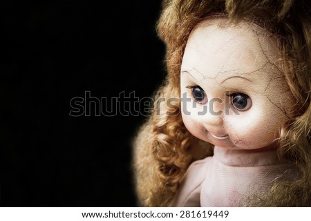 Face of baby girl scary doll on black dark background. devil vintage toy creepy party festival night light smile display dark faith halloween cracks demons evil.