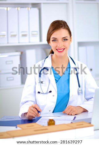 Beautiful young smiling female doctor sitting at the desk 