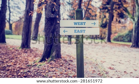 Vintage Wooden Signpost at the Quiet Park for West and East Directions Concept.