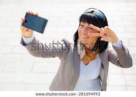 Stylish woman 30 years, smiling pretty woman taking pictures selfie her phone and have fun, dressed in suit, sunny day, city street, soft light series, Positive emotion, facial expression, spring mood