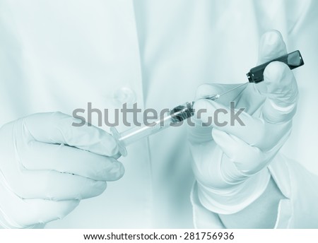 Hands in gloves filling medicine from ampule into syringe against the background of medical robe. Toned.