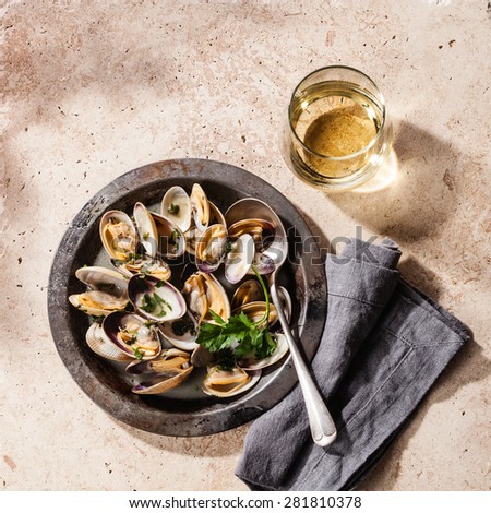 Shells vongole venus clams in metal dish and wine on stone background