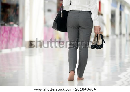 Young woman in office style clothes carrying in hand her high heel shoes, walking barefoot in contemporary building, legs close-up Royalty-Free Stock Photo #281840684