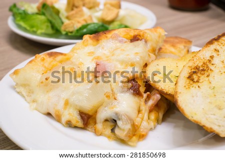 Closeup view of an appetising ham and pineapple Italian pizza with garlic bread and salad