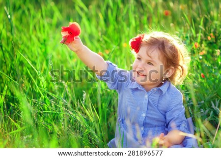 Beautiful baby girl walking in a sunny garden with a flower