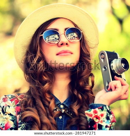 Outdoor summer lifestyle portrait of pretty young woman having fun in the city. Photographer making pictures in hipster style glasses and hat. Photo toned style Instagram filters.