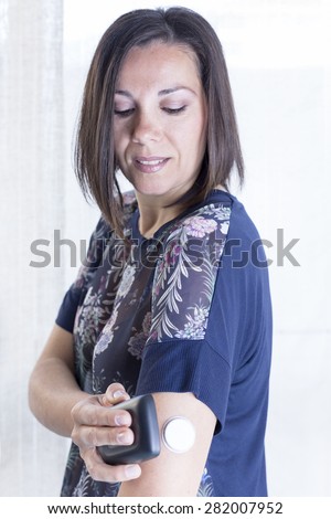 young woman is scanning the sensor of the glucose monitoring system at the back of her arm with the reader at home - focus on the woman face Royalty-Free Stock Photo #282007952