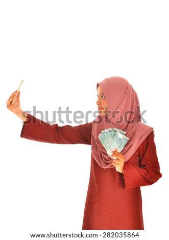 A smiling muslim woman holding money while taking self potrait picture, isolated on white background. 