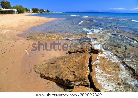 Aegean sea shore with sandy beach and flat underwater rocks, Greece