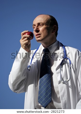 Doctor wearing laboratory coat, with stethoscope and holding an apple, to keep the doctor away, with a great blue sky behind him