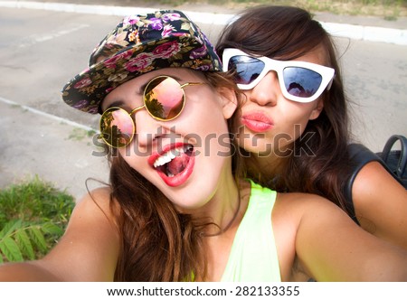Close up lifestyle portrait of two pretty fresh hipster young brunette and blonde best friends girls,make selfie and having fun.Wear summer sunglasses and make photos,of their weekends.Selfie portrait