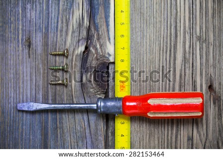 old screwdriver, three screws and measuring tape on the boards of the old bench