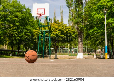 Forgotten Basketball on Empty Court in Park Filled with Green Trees