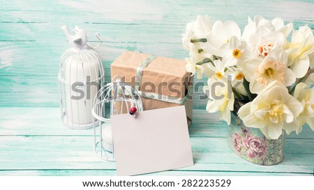 Background with colorful narcissus flowers , candles, box with present  and empty tag for text on turquoise painted wooden planks. Selective focus. Place for text. Toned image.