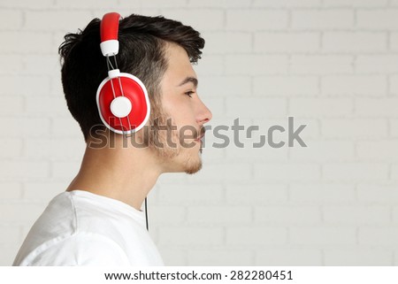 Handsome young man listening to music on brick wall background background