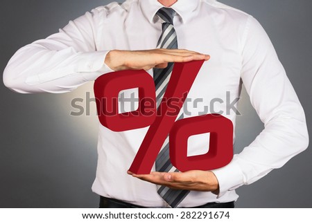Adult businessman holding 3 D percent sign, isolated on dark background. 