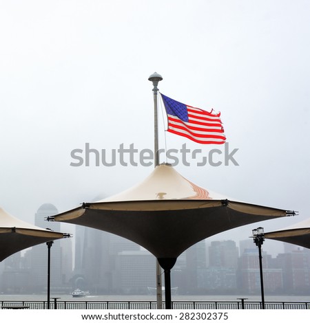 Tattered American flag blowing in the wind with Manhattan skyline on background on a rainy day