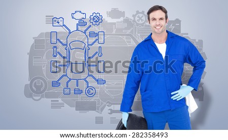Mechanic holding tire while standing with hand on hip against grey vignette