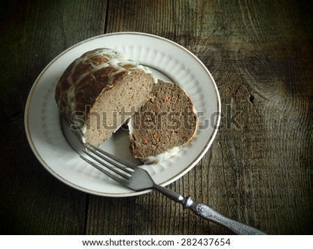Homemade goose pate in a natural casing on a vintage white plate on raw wooden background. Grunge style.