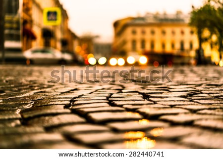 City central square paved with stone after a rain, headlights from cars in the distance. View from the pavement level, image in the yellow toning