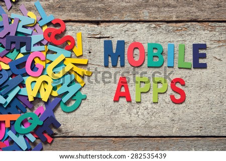 The colorful words "MOBILE APPS" made with wooden letters next to a pile of other letters over old wooden board. 
