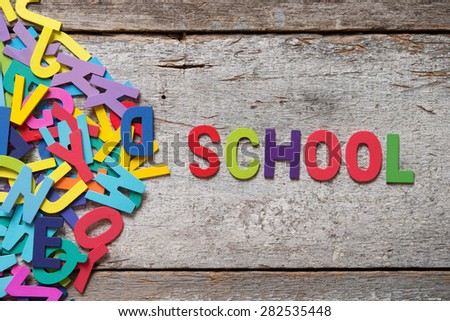 The colorful words "SCHOOL" made with wooden letters next to a pile of other letters over old wooden board.