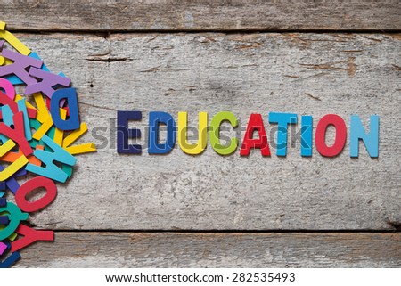 The colorful words "EDUCATION" made with wooden letters next to a pile of other letters over old wooden board.