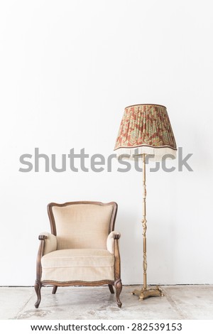 Beige vintage armchair and lamp on white wall.