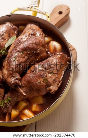 High Angle View of Roasted Rabbit Haunch with Stewed Vegetables in Pan Garnished with Fresh Herbs on Cutting Board
