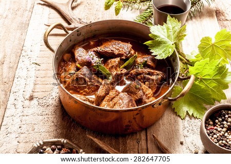 Venison Goulash Stew in Copper Pot with Bowls of Seasoning on Wooden Surface Surrounded by Deer Antlers and Leaves Royalty-Free Stock Photo #282647705