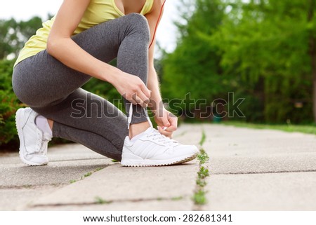 Tie it hard. Close up of pleasant young-looking lady lacing her sport shoes in park