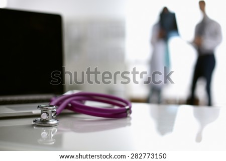 Laptop and medical stethoscope on the desk , doctors standing in the background.