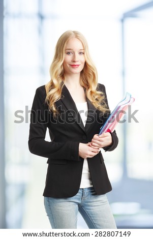 Portrait of a young smiling businesswoman holding files in hand while standing at office