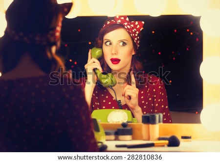 Portrait of a beautiful surprised woman with a dial phone and applying cosmetics near a mirror. Photo in retro color style.