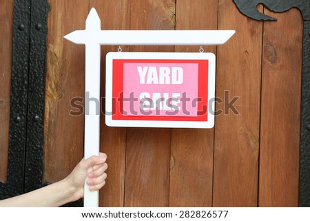 Wooden Yard Sale sign in female hand on wooden fence background