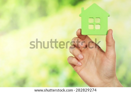 Female hand holding house on green blurred background