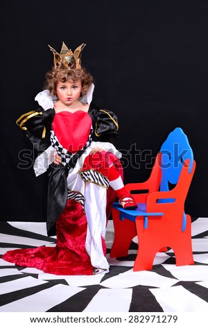 Expressive discontented little girl in the image of the Red Queen, with a crown on her head and heart on her dress.