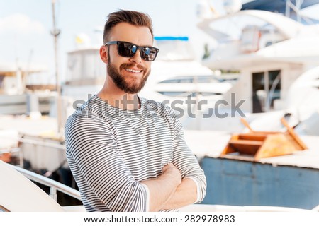 Confident yachtsman. Smiling young man keeping arms crossed and looking at camera while standing on the board of yacht  Royalty-Free Stock Photo #282978983