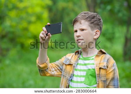 A boy is taking photo by mobile phone in summer park