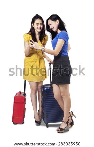 Full length of pretty female tourists using cellphone to see a map while carrying luggage in studio