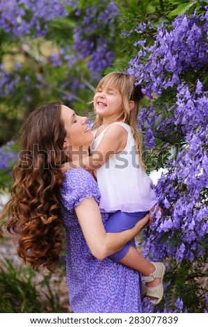 Young beautiful mother and her cute daughter love in blooming jacaranda garden