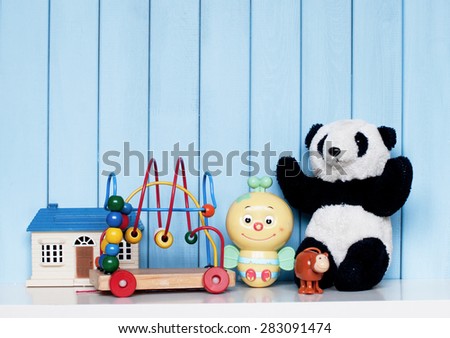 Toy house, old vintage panda, mechanical bee, clockwork monkey and spiral labyrinth on the bookshelf in the children's room on blue wooden background