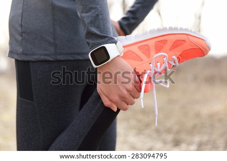 Running stretching - runner wearing smartwatch. Closeup of running shoes, woman stretching leg as warm-up before run with sport activity tracker watch at wrist to monitor the heart rate during cardio. Royalty-Free Stock Photo #283094795