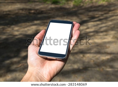 Front view of holding on hand black smartphone with white blank screen in forest.