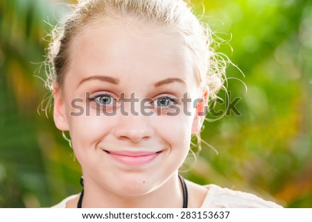 Closeup outdoor portrait of beautiful happy blond Caucasian teenage girl in a summer park