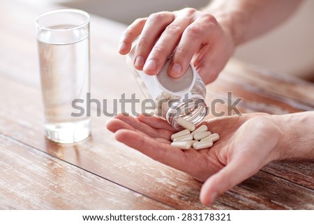 sport, healthy lifestyle, medicine, nutritional supplements and people concept - close up of man with glass of water pouring pills from jar to hand Royalty-Free Stock Photo #283178321