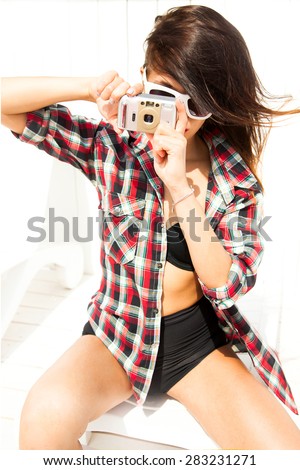 Outdoor lifestyle portrait of pretty young lady having fun and  take pictures on the beach in evening with travel camera,retro photo of photographer.hipster style sunglasses,bikini store,white,adult
