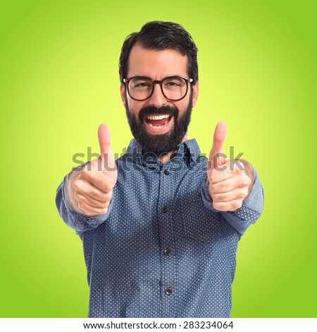 Young hipster man with thumb up over colorful background