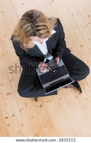 A business woman sitting cross-legged on the floor using a pda with a laptop on her knees