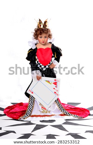 Funny discontented little girl in the image of the Red Queen, with a crown on her head and heart on her dress, holds giant  playing cards